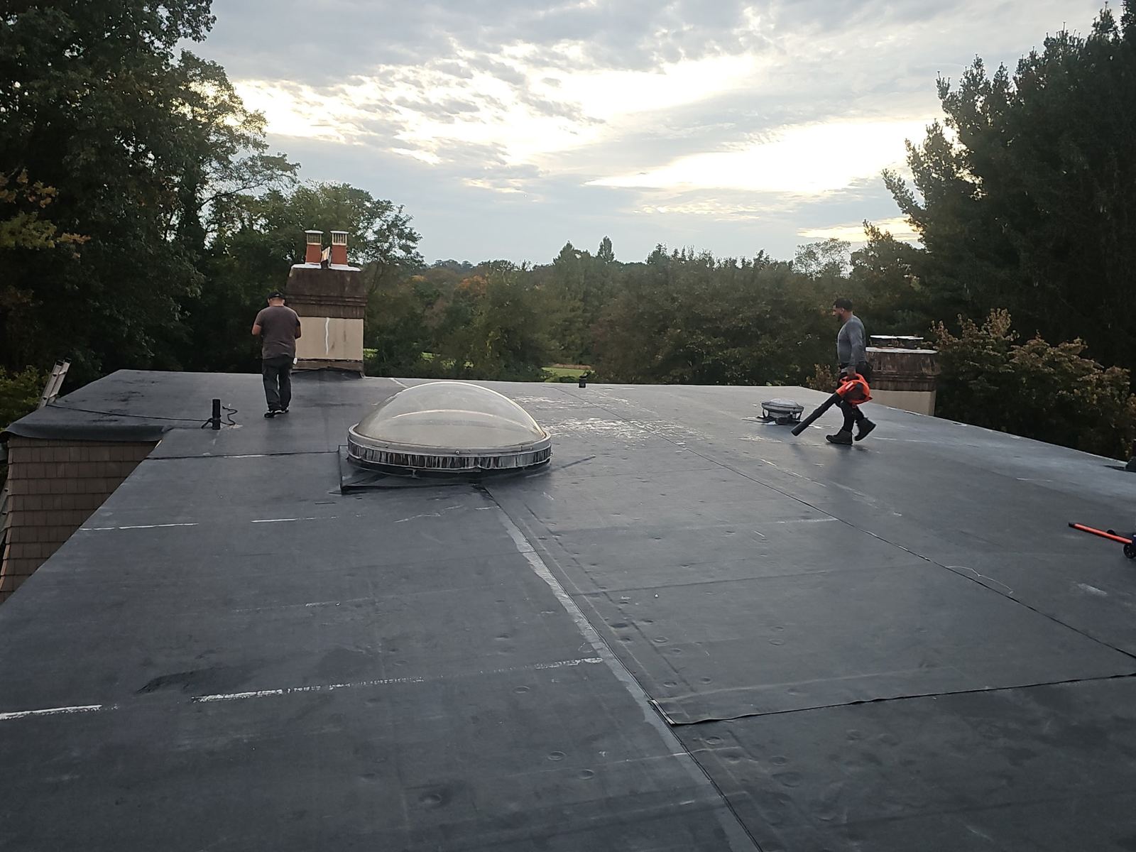 Finished black membrane flat roof with skylight and crew cleaning up